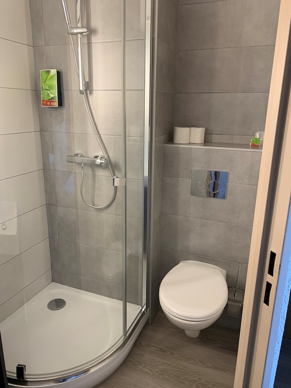 Un baño moderno con ducha de vidrio, inodoro y un pequeño estante con artículos de aseo.