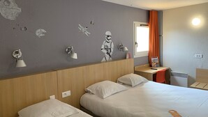 A hotel room with two beds, a wall with Star Wars-themed decorations, a bedside table with a lamp, and a window with orange curtains. - Brit Hotel Essentiel Tours Sud – Chambray-lès-Tours  (Chambray-les-Tours)