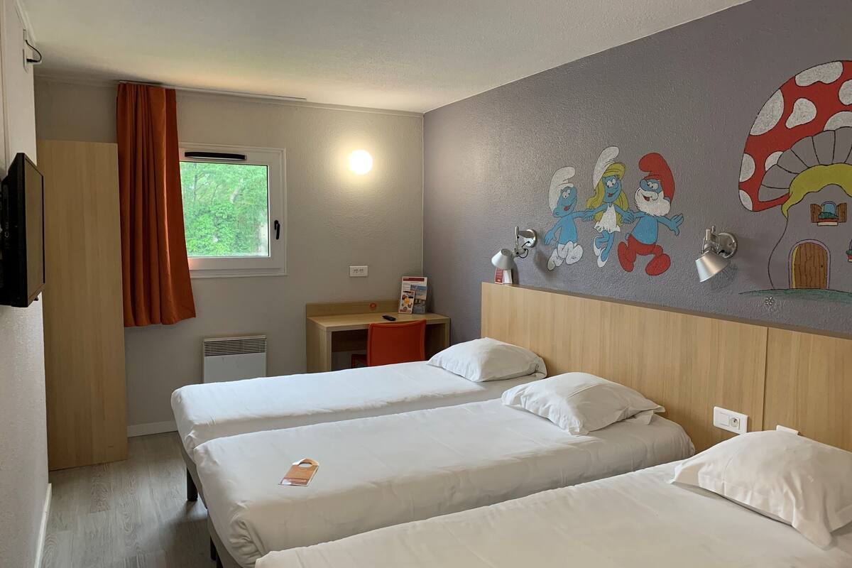 Ein Hotelzimmer mit zwei Betten, einem Schreibtisch, einem Stuhl, einem Fernseher und einem Fenster mit Vorhängen.