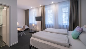 A hotel room with two beds, a desk, a chair, a TV, and large windows with curtains. -  BIG MAMA Leipzig (Leipzig)