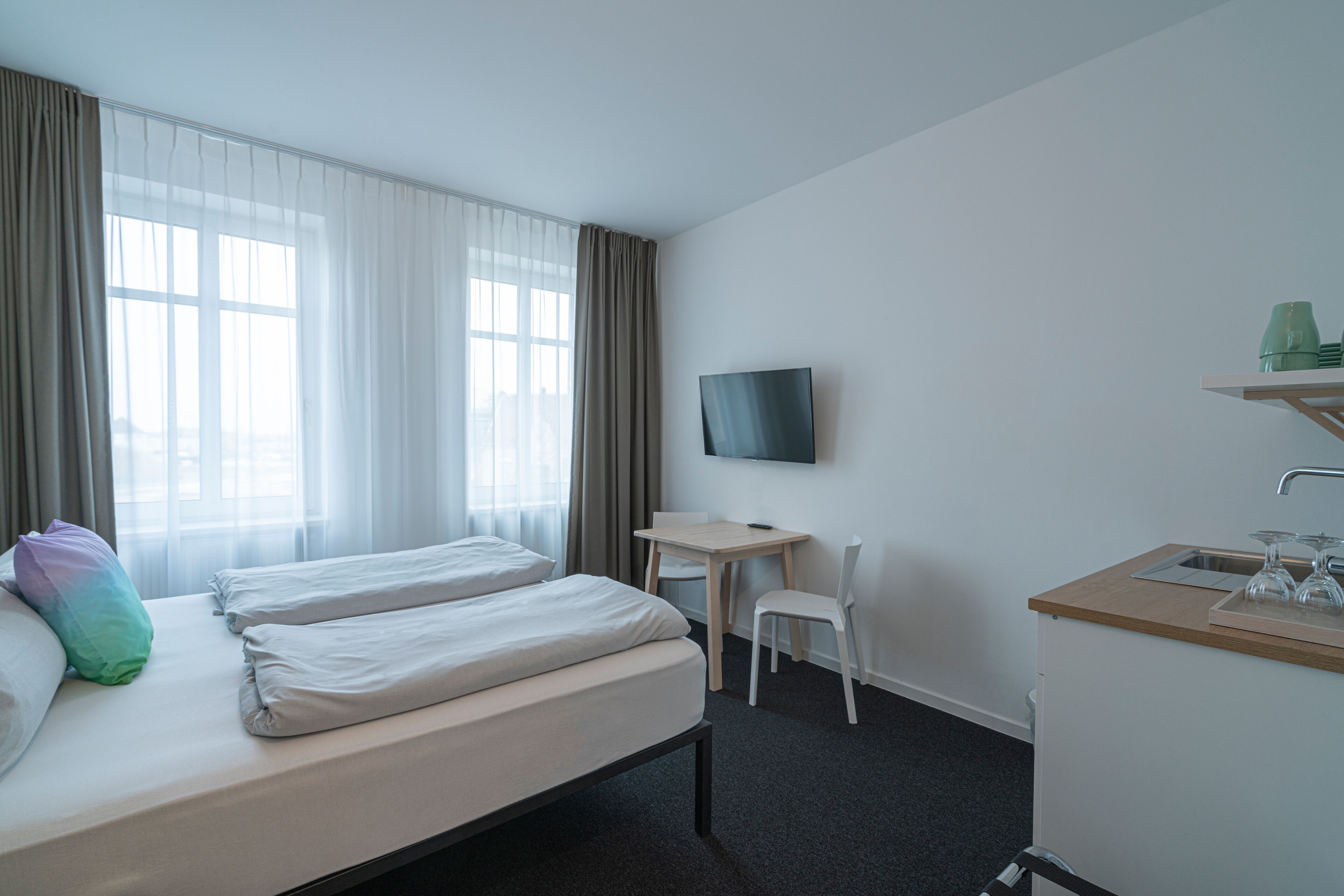Une chambre d’hôtel avec deux lits, un bureau, une chaise, une télévision et une kitchenette.
