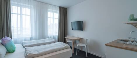 Une chambre d’hôtel avec deux lits, un bureau, une chaise, une télévision et une kitchenette.