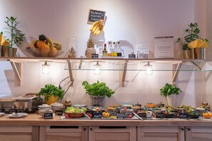 Monipuolinen buffet, jossa on useita ruokapisteitä, kuten hedelmäkulho, mausteita ja kyltti, jossa lukee: ”Big Maman kotitekoiset herkut perjantaisin”.