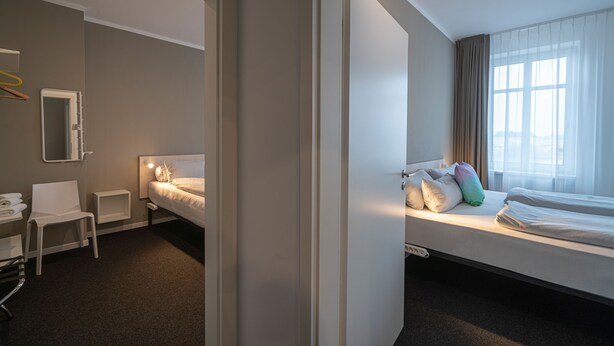 A hotel room with two beds, a desk, a chair, a mirror, and a window with curtains. -  BIG MAMA Leipzig (Leipzig)