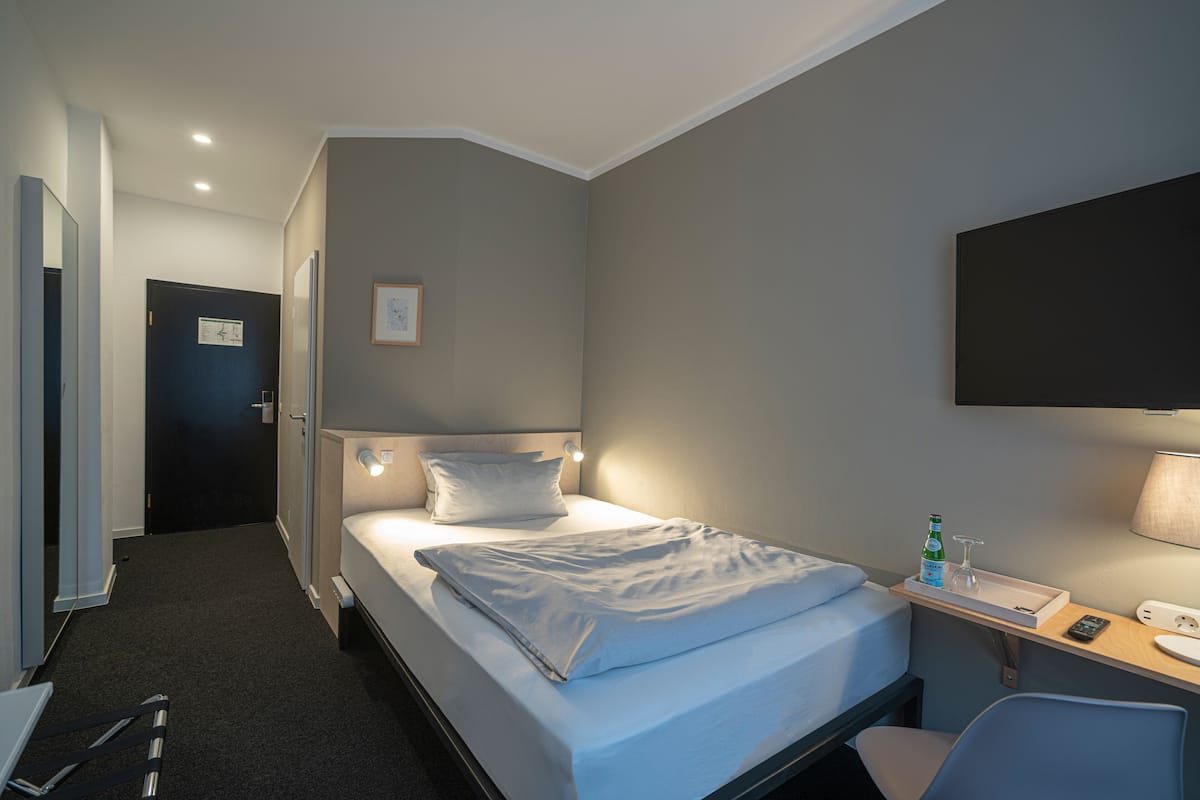 A hotel room with a bed, bedside table, chair, and a desk with a lamp.
