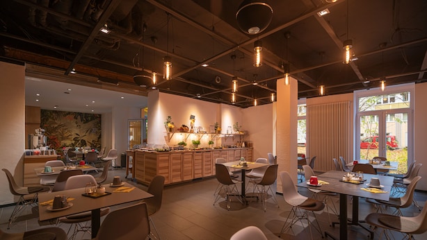 A modern dining area with multiple tables and chairs, a kitchen in the background, and large windows allowing natural light. -  BIG MAMA Leipzig (Leipzig)