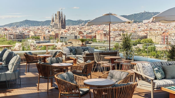 Une terrasse sur le toit, aménagée avec des meubles en osier, des parasols et offrant une vue sur le paysage urbain, notamment sur un bâtiment remarquable.