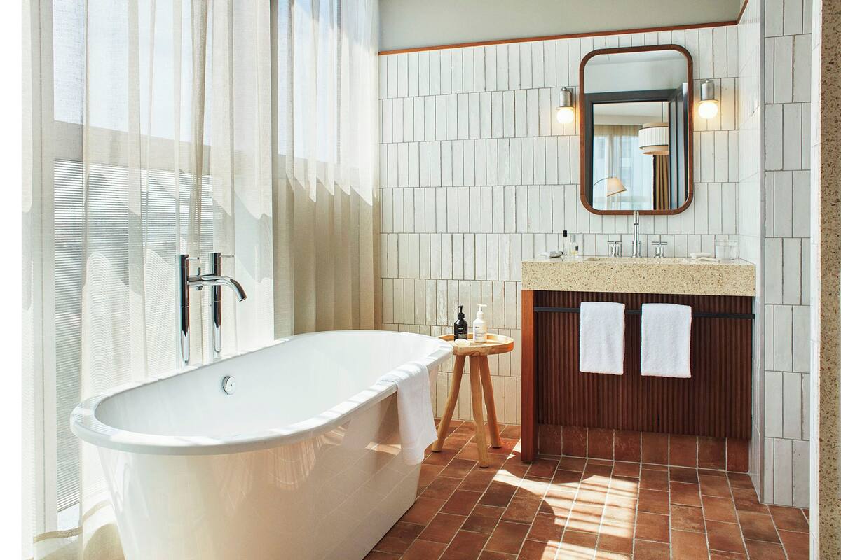 A modern bathroom with a freestanding bathtub, a wooden vanity, a mirror, and a towel rack.