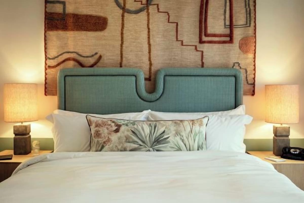 Una camera d'albergo con un letto grande, due lampade sui comodini e una testiera decorativa.