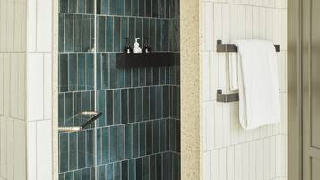 Un baño con azulejos azul oscuro, un toallero blanco y un estante negro con artículos de aseo.