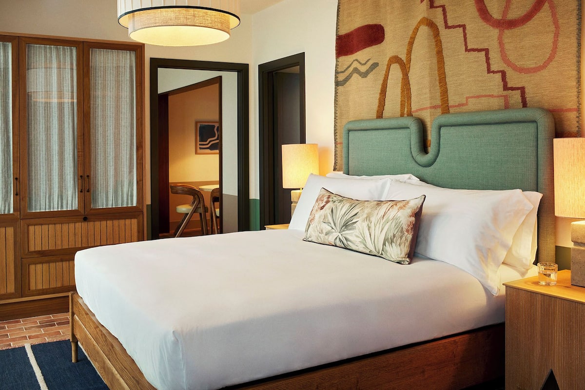 A hotel room with a large bed, wooden headboard, and a view of the hallway.