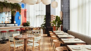 Un restaurant moderne avec un plancher en bois, des chaises à carreaux et différents types de sièges, notamment des tables rondes et un long banc.