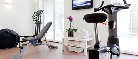 A home gym with a stationary bike, elliptical, and weight bench.