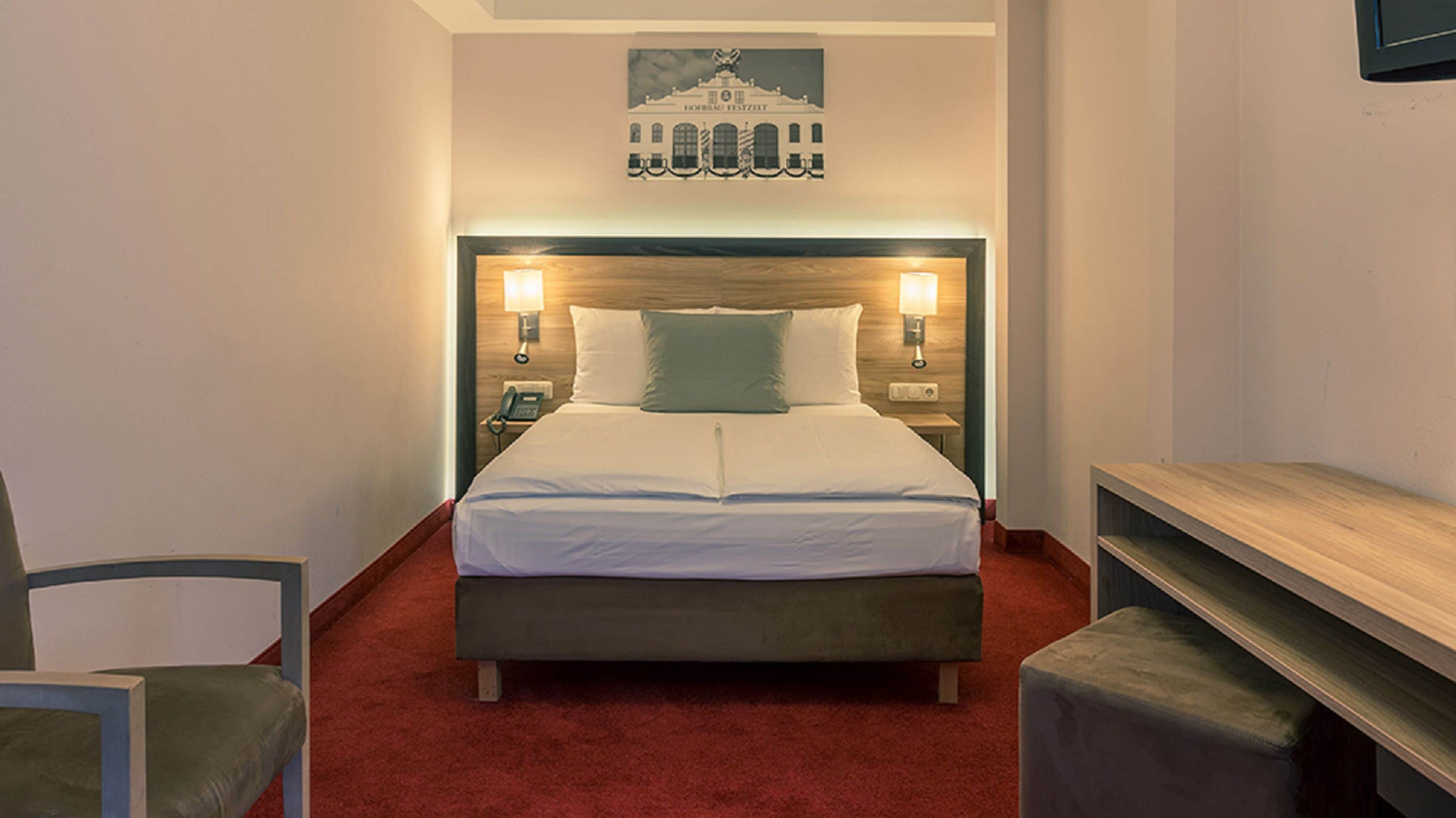 Une chambre d’hôtel avec un lit, deux tables de chevet, une chaise et un banc en bois.