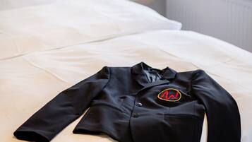 A neatly made bed with a black shirt on it, a small table with a plant, and a window with a view of the outside.