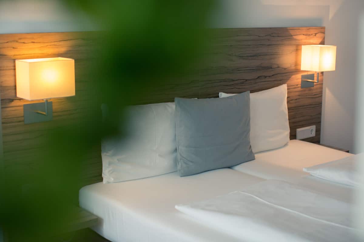 A neatly made bed with white linens and pillows, two wall-mounted lamps, and a wooden headboard.