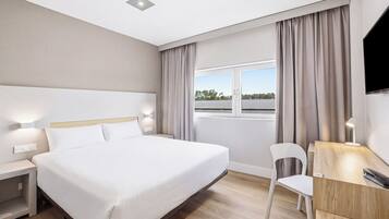 A hotel room with a large bed, a desk with a chair, a TV, and a window with curtains.