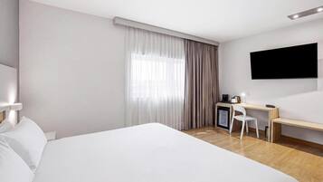 Habitación de hotel con una cama grande, un escritorio, una silla, un televisor y una ventana con cortinas.