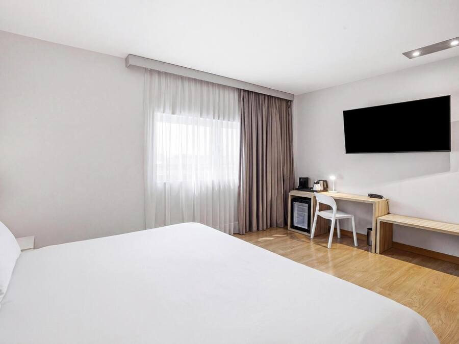 Habitación de hotel con una cama grande, un escritorio, una silla, un televisor y una ventana con cortinas.
