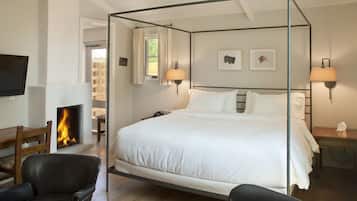 A four-poster bed with white linens, a fireplace, a television, and two wall-mounted lamps.