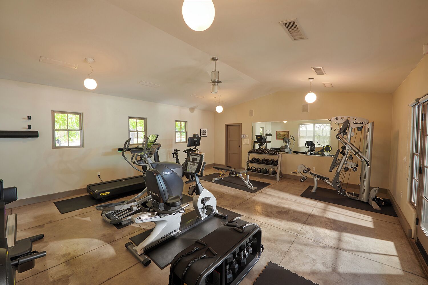 A gym with cardio machines, free weights, and a mirrored wall.