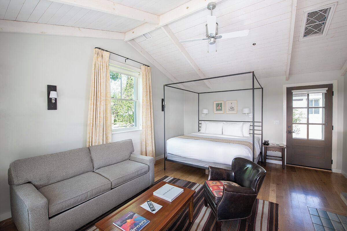 A bedroom with a four-poster bed, a sofa, a coffee table, and a door leading to another room.