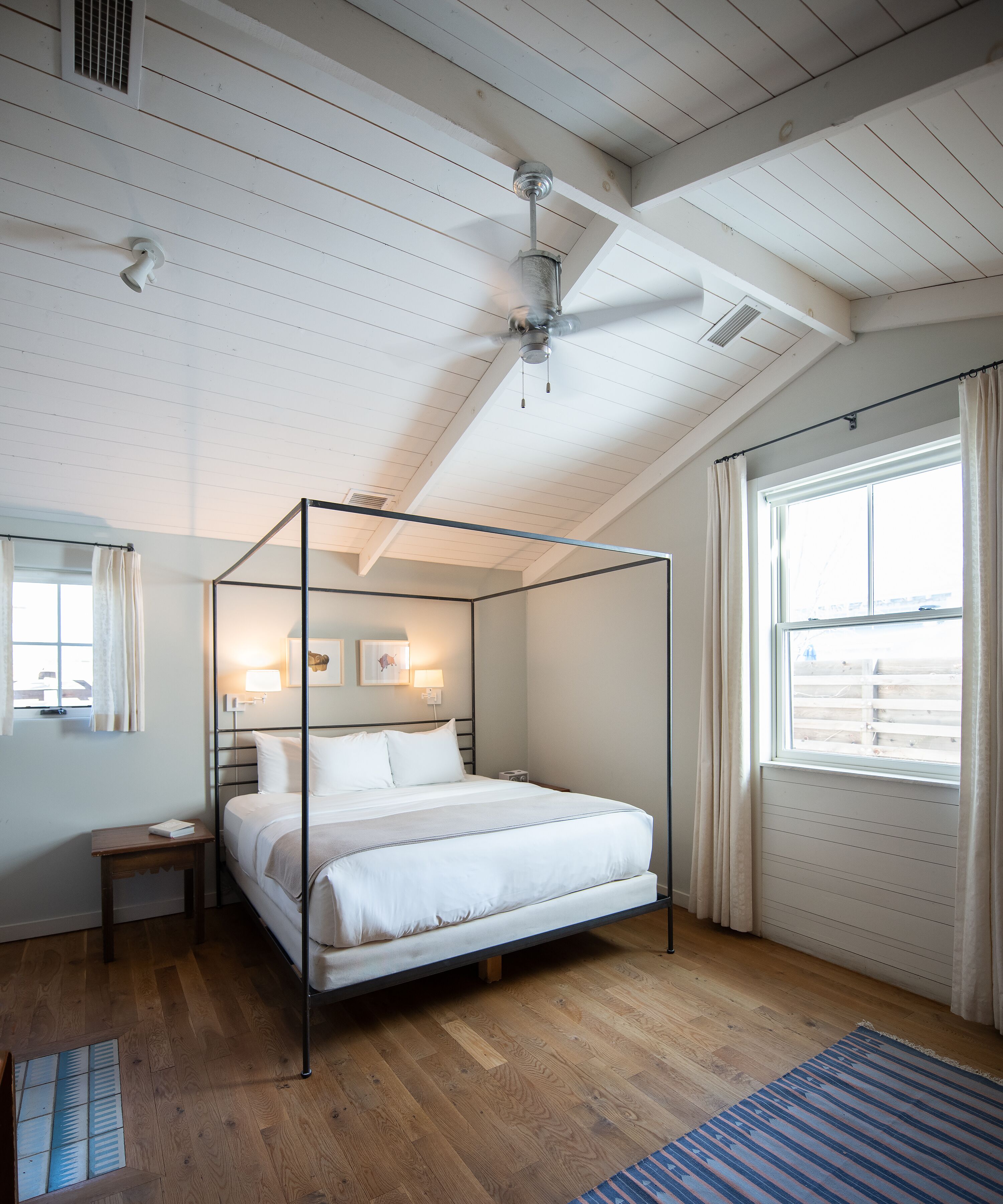 Ein Schlafzimmer mit einem Himmelbett, Deckenventilator, einem Fenster mit Vorhängen und Holzboden.