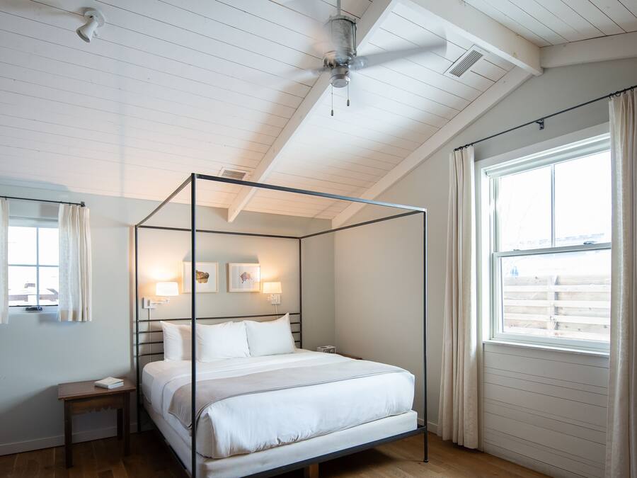 Ein Schlafzimmer mit einem Himmelbett, Deckenventilator, einem Fenster mit Vorhängen und Holzboden.