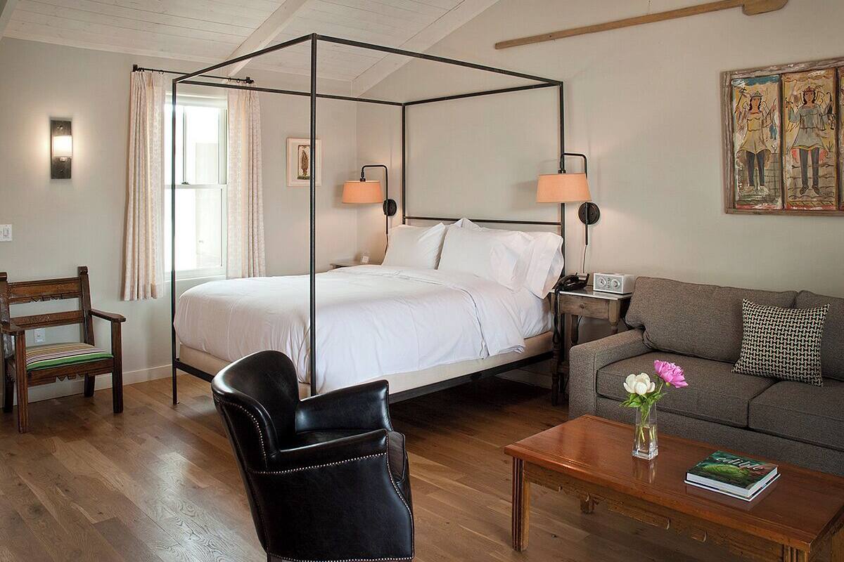 A four-poster bed with a wooden frame, a sofa, a coffee table, a chair, and a painting on the wall.