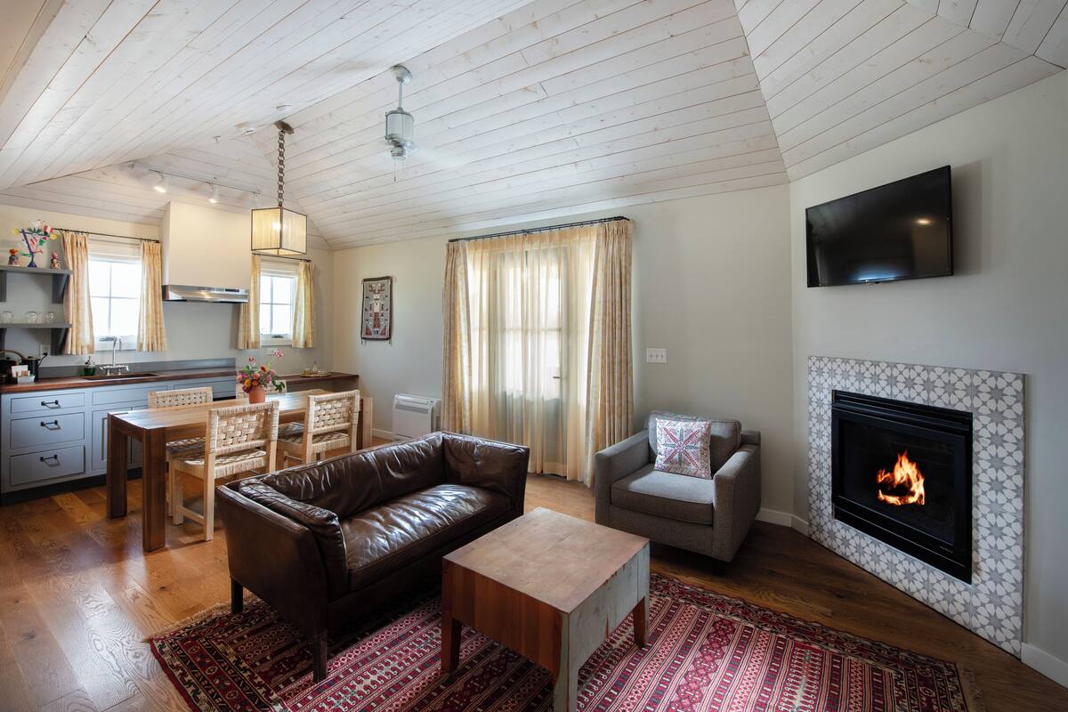 A cozy living room with a fireplace, a dining area with a wooden table and chairs, and a kitchen with a modern design.
