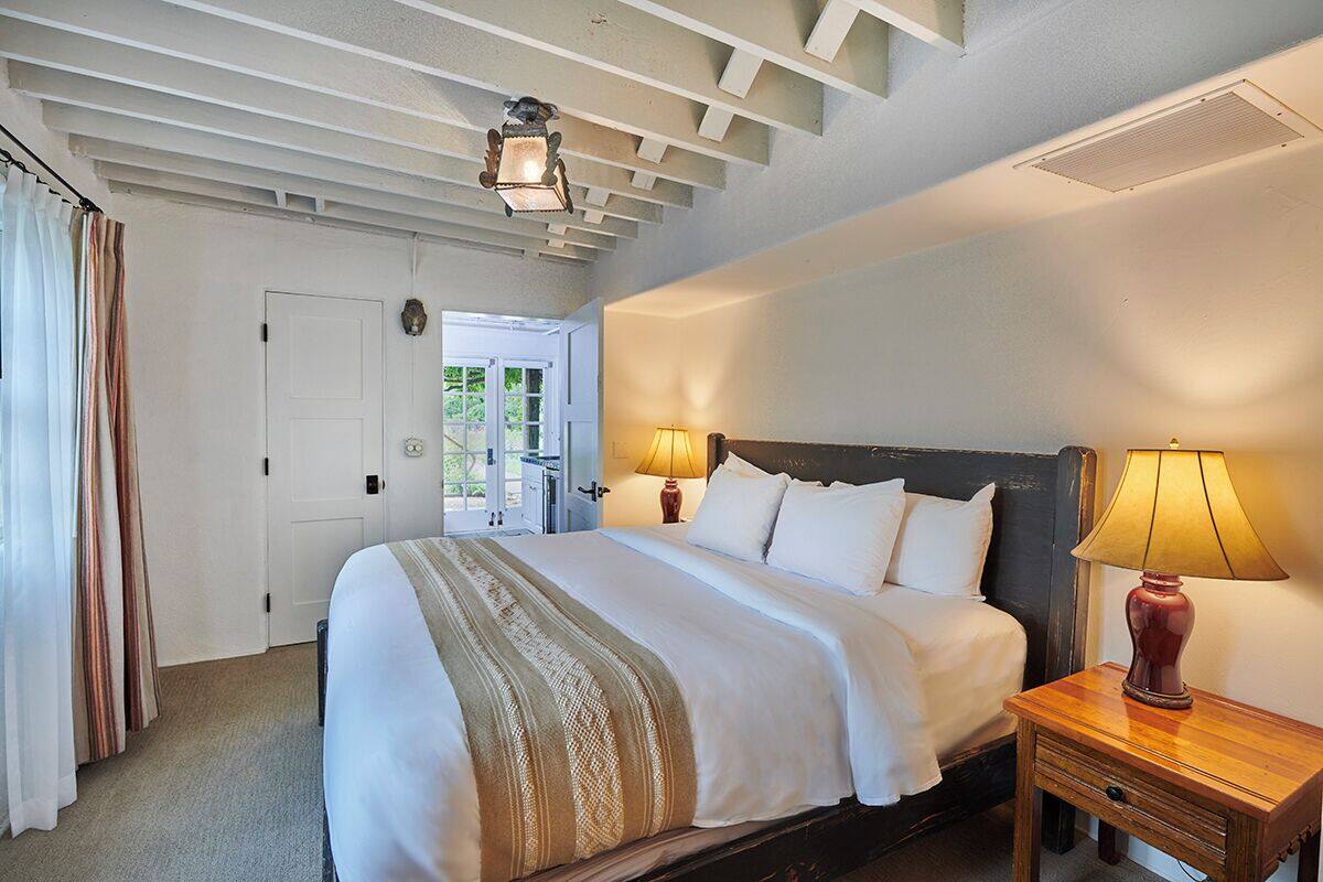 A bedroom with a large bed, two bedside lamps, a wooden nightstand, and a door leading to a balcony.