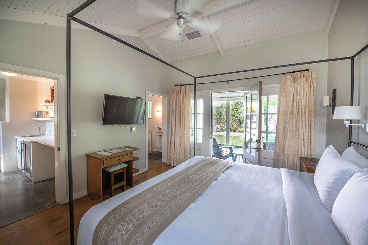 A bedroom with a large bed, a desk, a television, and a view of the outdoors.