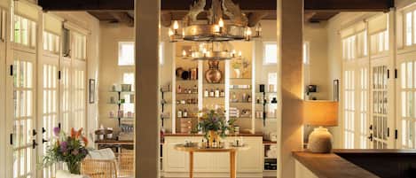 A well-lit room with a wooden ceiling, a chandelier, wicker furniture, and a central table with a vase of flowers.