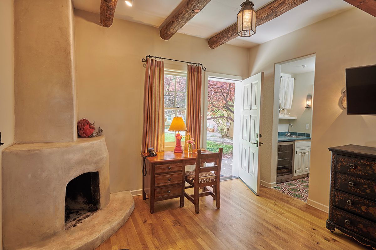 A room with a fireplace, wooden desk, chair, and a television mounted on the wall.