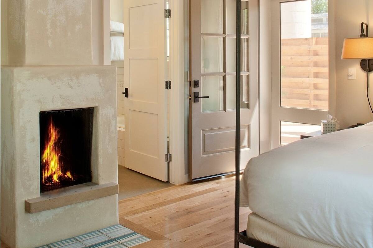 A bedroom with a four-poster bed, a fireplace, and a large window.