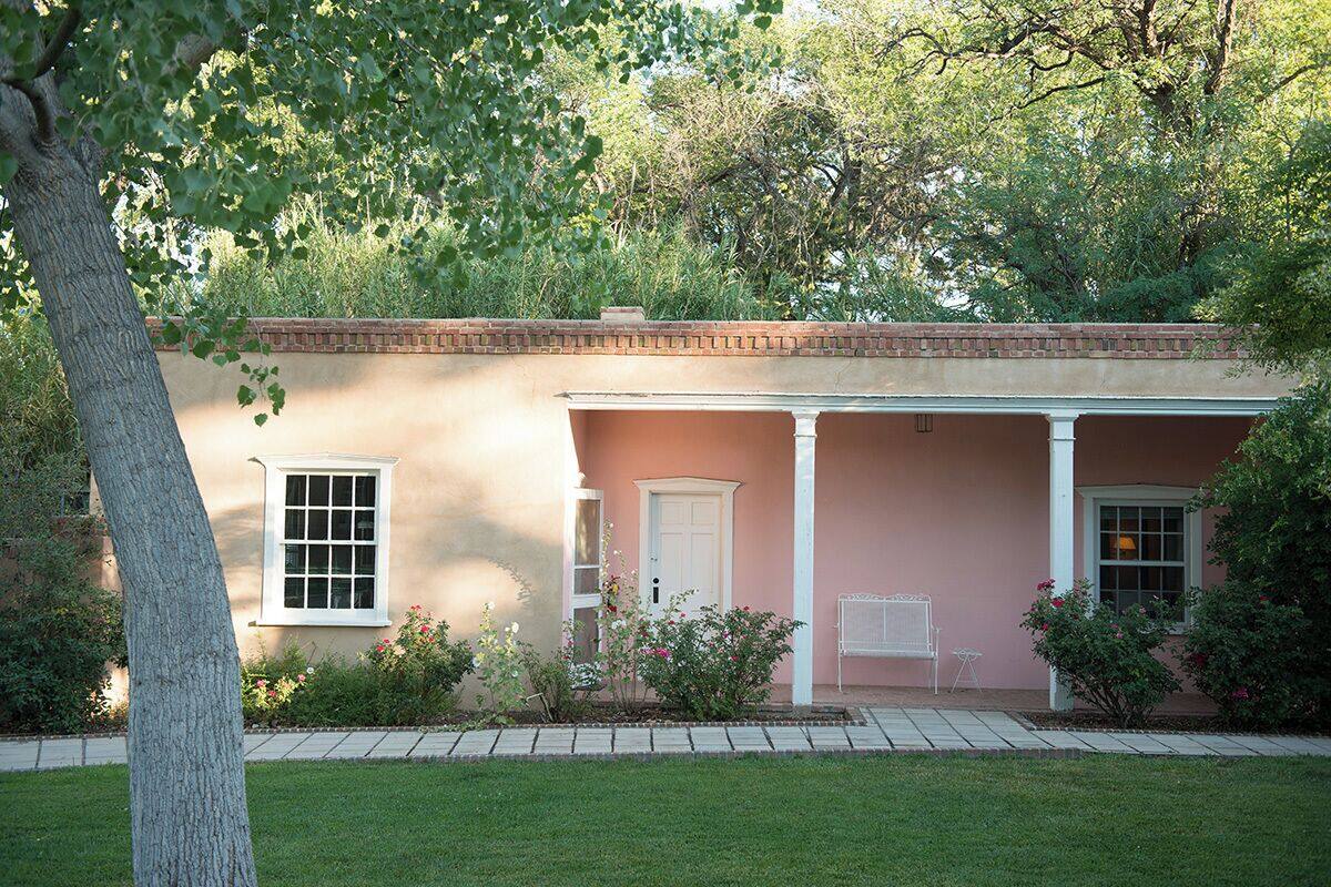 A house with a brick facade, a porch with white columns, and a small garden with various plants and flowers.