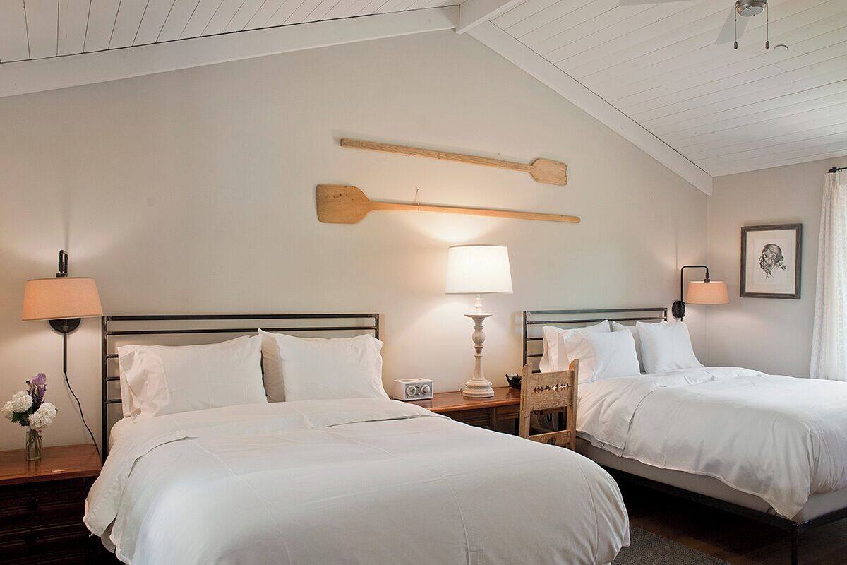 A hotel room with two beds, wooden headboards, bedside lamps, a small table with a radio, and a framed picture on the wall.