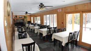 Ein Restaurant mit mehreren Tischen, Stühlen, einem Deckenventilator und großen Fenstern.