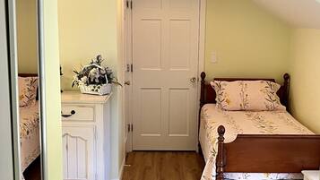 A bedroom with a wooden floor, a bed with floral bedding, a nightstand, a dresser, and a mirror.