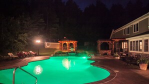Ein Schwimmbad mit Gazebo, einer überdachten Terrasse und einem Haus mit Veranda.