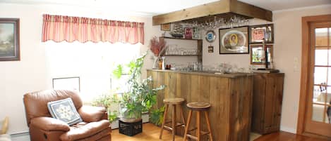 A cozy living room with a brown leather chair, a round coffee table, wooden stools, a wooden bar area with glasses and a potted plant.