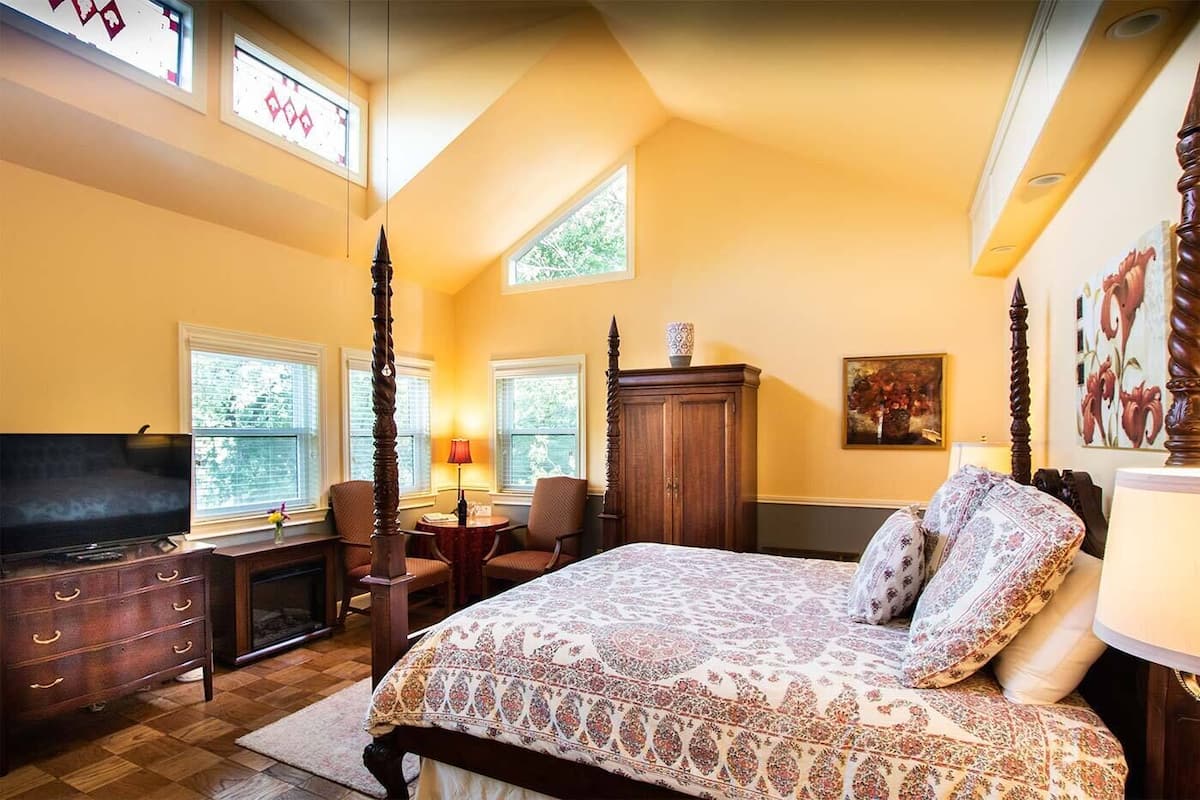 A bedroom with a large bed, a TV, a wooden dresser, and a desk with chairs.