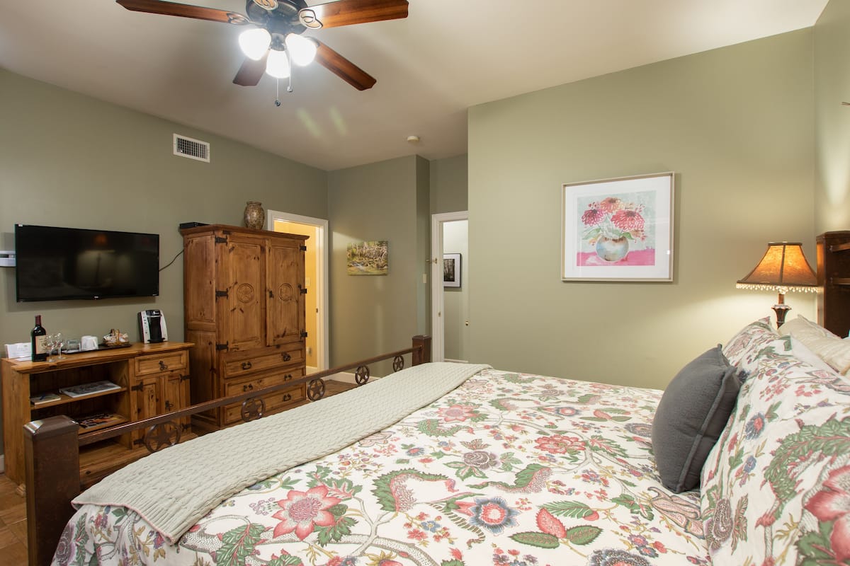 A bedroom with a bed, wooden dresser, television, and artwork on the walls.