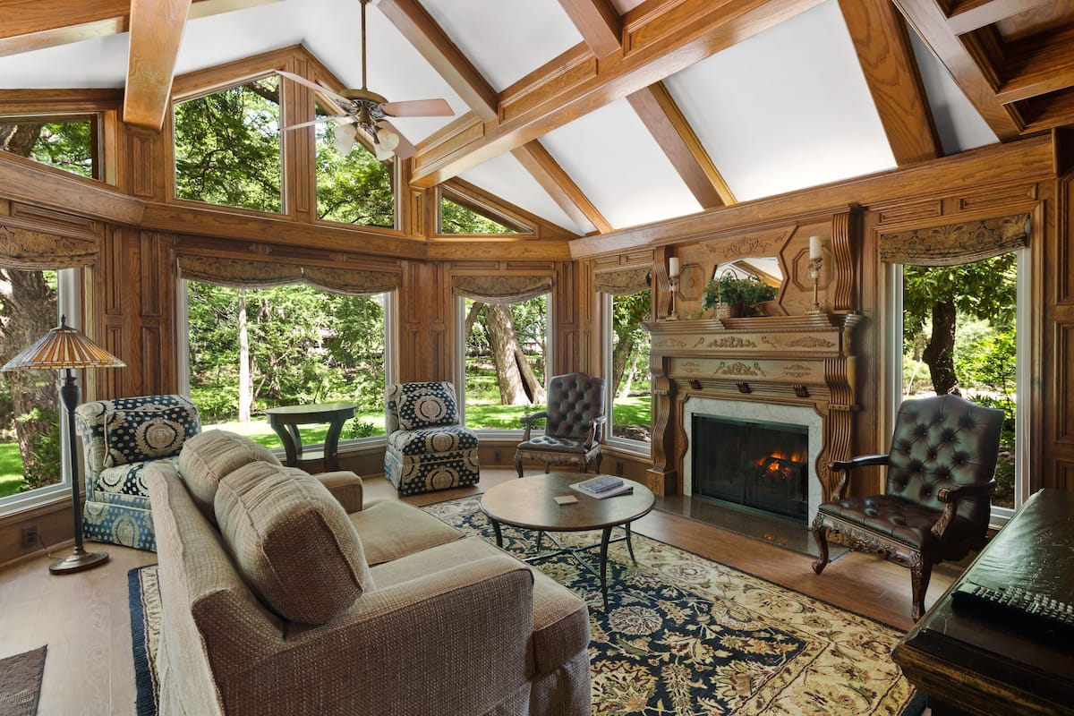 A spacious living room with a fireplace, large windows, and a ceiling fan.