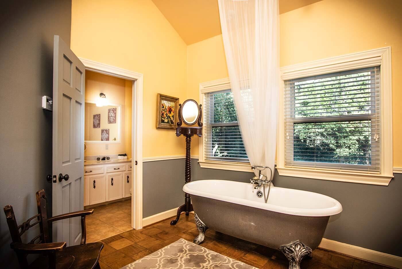 A bathroom with a freestanding bathtub, a vanity with a mirror, and a window with blinds.
