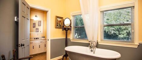 A bathroom with a freestanding bathtub, a vanity with a mirror, and a window with blinds.