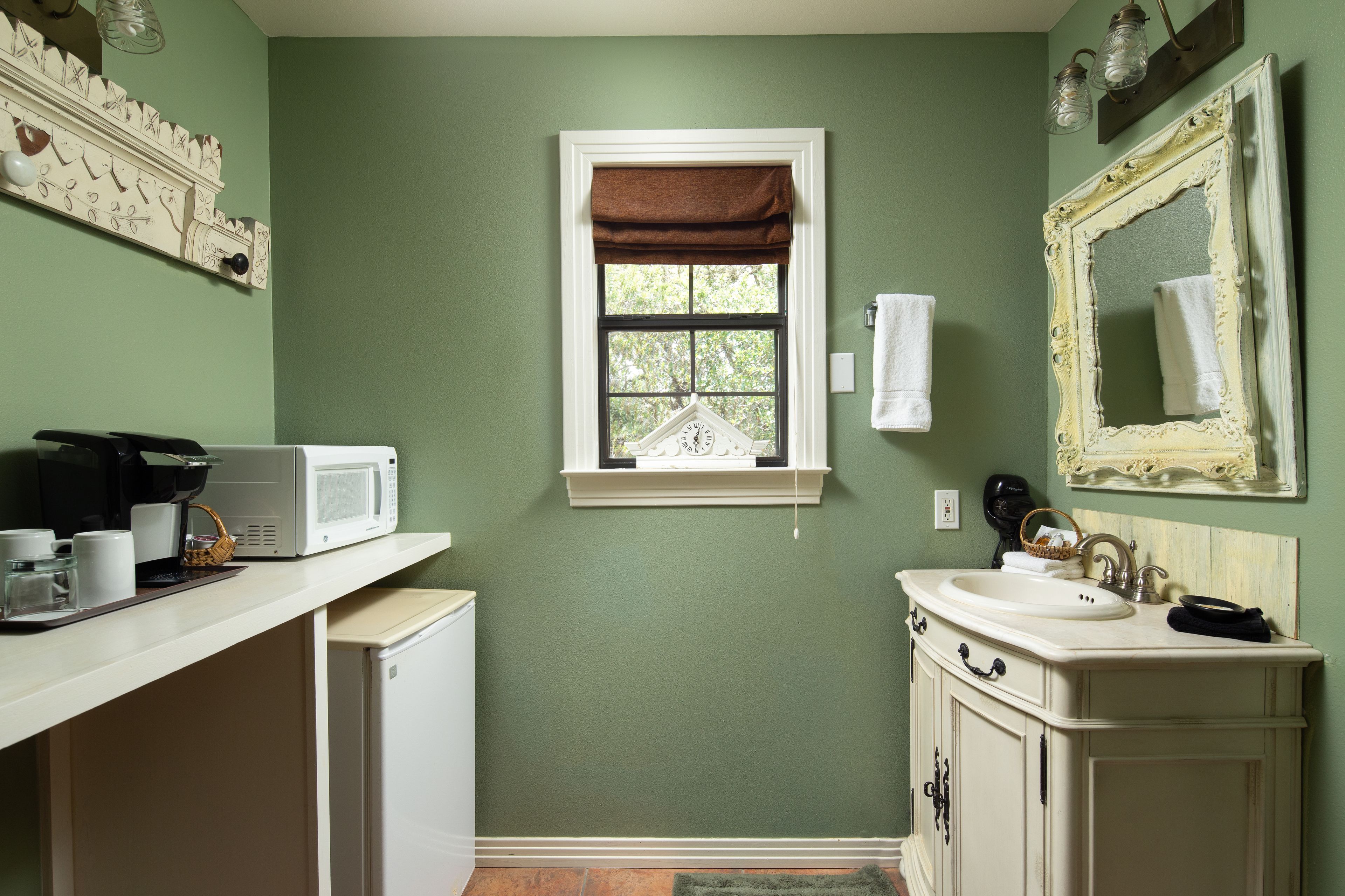 A bathroom with a green wall, a white sink, a mirror, and a window with a brown valance.