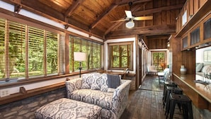 A wooden interior with a sofa and ottoman, large windows, and a ceiling fan. - Creekhaven Inn & Spa (Wimberley)