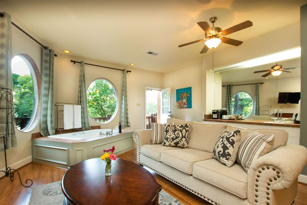 A spacious living room with a large window, a ceiling fan, a sofa with patterned cushions, and a wooden coffee table.