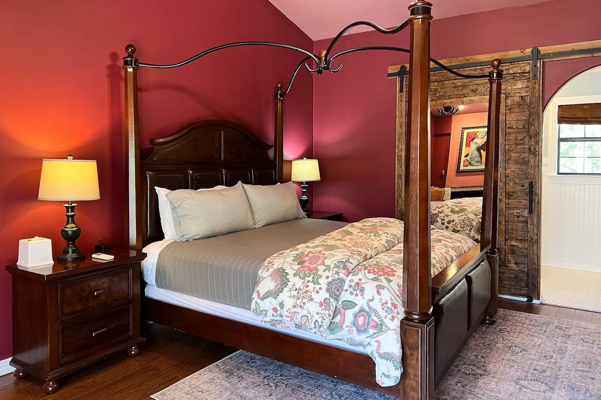 A four-poster bed with a floral bedspread, two bedside lamps, and a wooden nightstand with a tissue box.